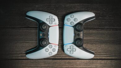 Two gaming controllers aligned symmetrically on a dark wooden surface, top view.