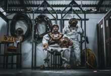 Two men in vintage dive suits pose indoors with equipment, Callao, Peru.