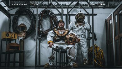 Two men in vintage dive suits pose indoors with equipment, Callao, Peru.