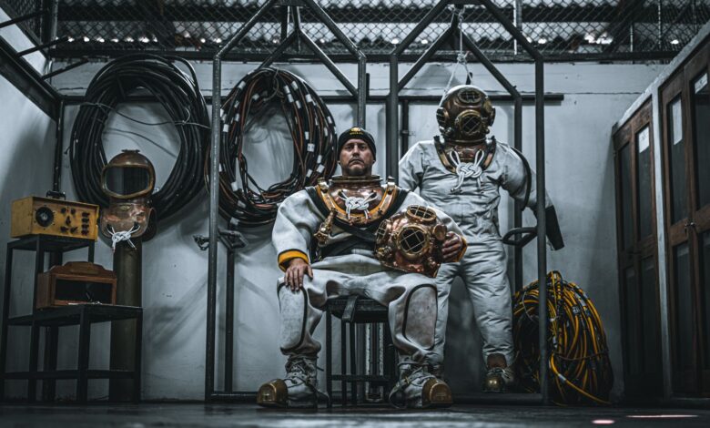 Two men in vintage dive suits pose indoors with equipment, Callao, Peru.