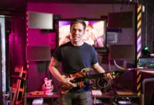 Adult male playing guitar controller in a vibrant gaming setup indoors, showcasing esports and recreation.