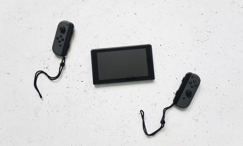 Flat lay of a Nintendo Switch and controllers on a white speckled surface, showcasing modern gaming tech.