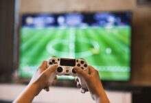 Close-up of hands holding a game controller playing a football video game on screen.