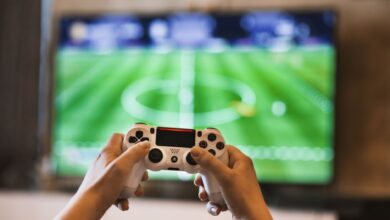 Close-up of hands holding a game controller playing a football video game on screen.