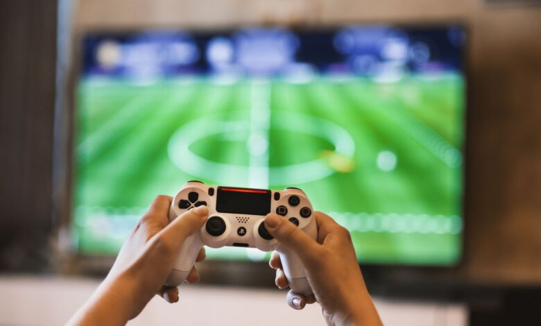 Close-up of hands holding a game controller playing a football video game on screen.