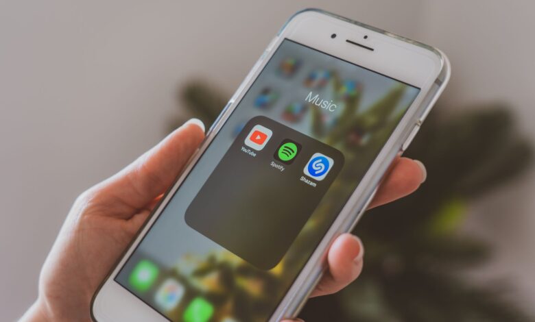 Hand holding a smartphone displaying popular music apps like Spotify and Shazam in a close-up shot.