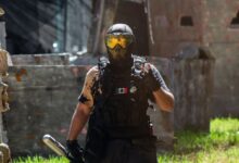 Armed paintball player with helmet and tactical gear in dynamic outdoor setting.