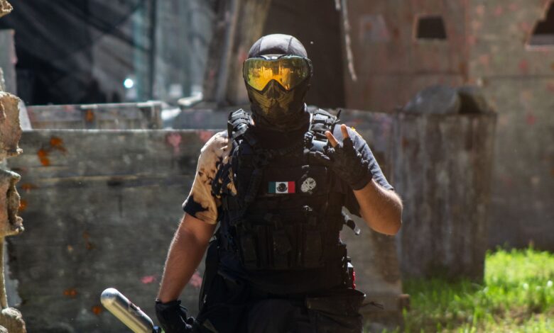 Armed paintball player with helmet and tactical gear in dynamic outdoor setting.