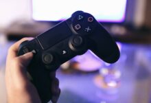 Person holding a gaming controller, blurred screen in background.