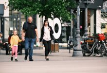 A family walks past storefronts and bicycles in a lively shopping district.