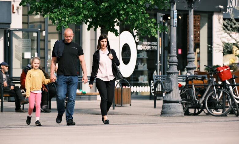 A family walks past storefronts and bicycles in a lively shopping district.