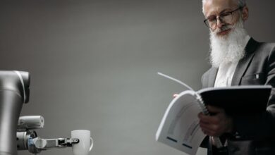 Elderly man reads as a robotic arm holds a coffee cup, showcasing technology integration.