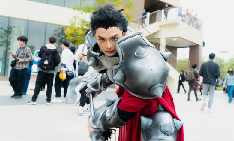 Man in intricate fantasy armor posing at a vibrant outdoor cosplay event.