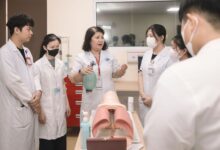 Group of medical students practicing skills with a training mannequin in a classroom setting.