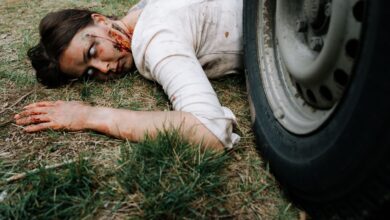 A chilling portrayal of a zombie with realistic makeup, lying near a tire.