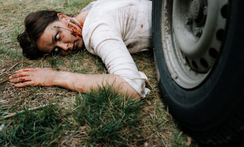 A chilling portrayal of a zombie with realistic makeup, lying near a tire.