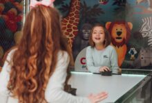 Two happy young girls playing air hockey indoors with colorful animal mural background.