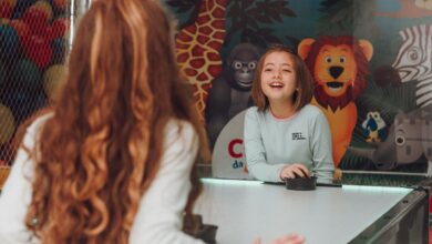 Two happy young girls playing air hockey indoors with colorful animal mural background.