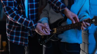 Two young adults playing an electric guitar together in a cozy indoor setting, showcasing teamwork and learning.