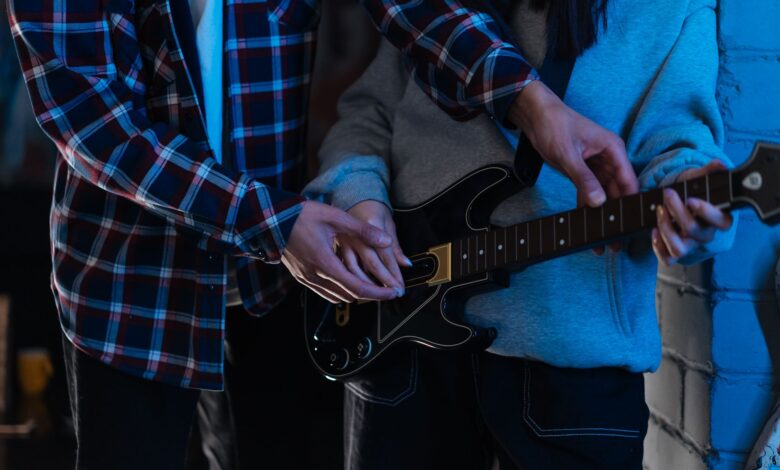Two young adults playing an electric guitar together in a cozy indoor setting, showcasing teamwork and learning.