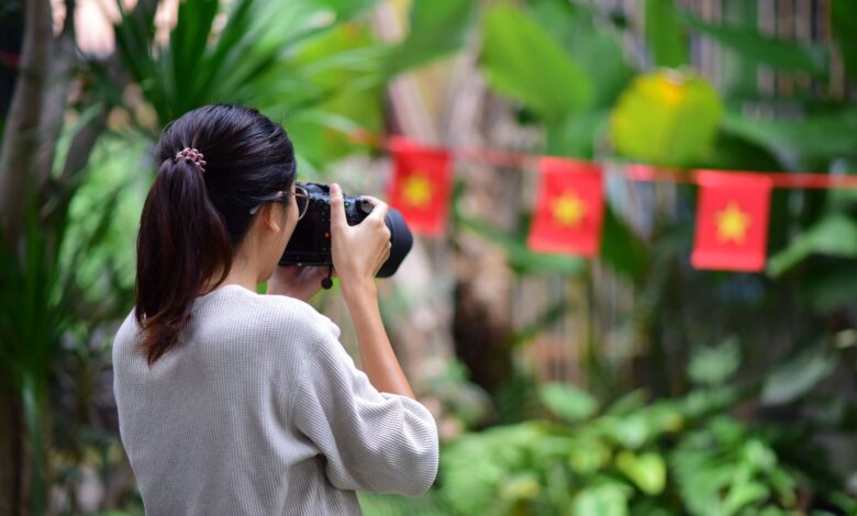 A woman takes photos in a lush outdoor setting with flags in the background.