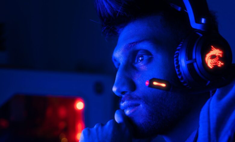 Close-up of a focused gamer with headset in blue lighting, embodying intense concentration.