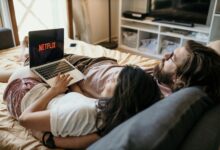 A cozy couple lounging in bed, streaming Netflix together on a laptop, enjoying a peaceful moment.
