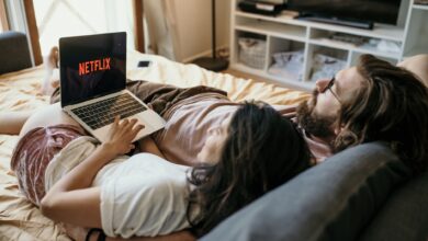 A cozy couple lounging in bed, streaming Netflix together on a laptop, enjoying a peaceful moment.