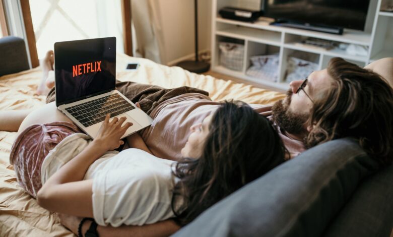 A cozy couple lounging in bed, streaming Netflix together on a laptop, enjoying a peaceful moment.