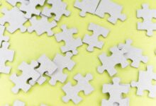 Close-up of gray puzzle pieces scattered on a vibrant yellow background for a playful abstract composition.