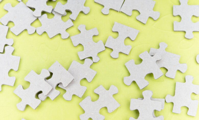 Close-up of gray puzzle pieces scattered on a vibrant yellow background for a playful abstract composition.
