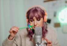 Woman with purple hair recording ASMR using a microphone and colorful props.