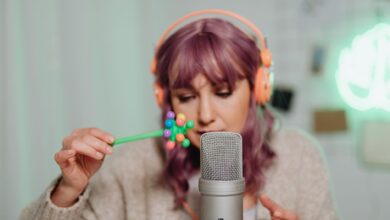 Woman with purple hair recording ASMR using a microphone and colorful props.