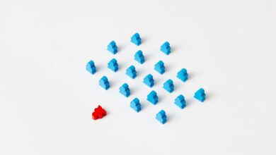 A distinctive red game piece stands out among blue meeples on a minimalist white background, symbolizing individuality.
