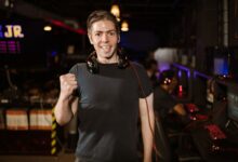 Smiling man with headphones and fist raised, celebrating in a gaming arena.