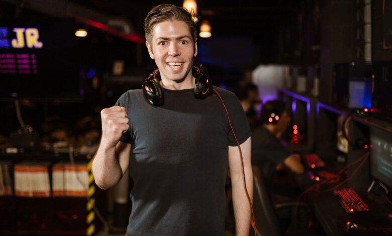 Smiling man with headphones and fist raised, celebrating in a gaming arena.