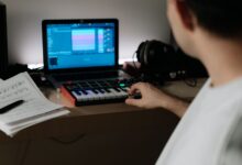 A music producer uses a synthesizer and laptop for composing in a home studio.