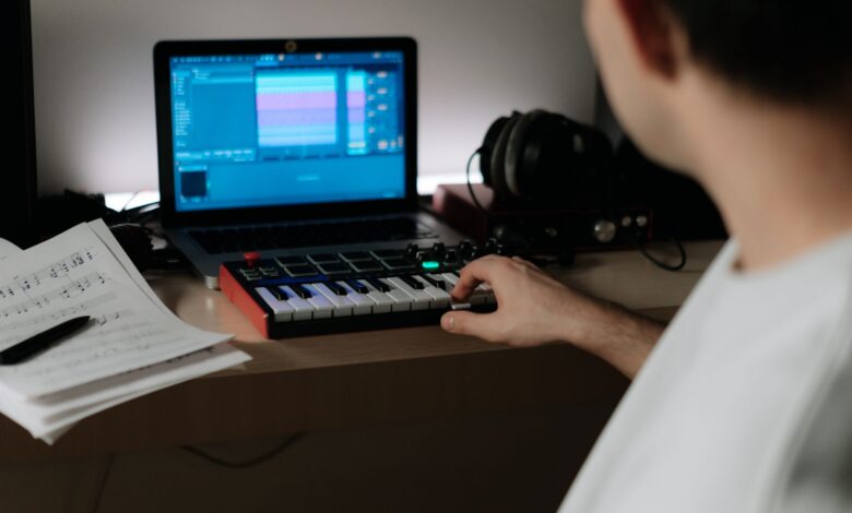 A music producer uses a synthesizer and laptop for composing in a home studio.