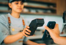 A cashier processes a contactless payment using a smartphone and card reader.
