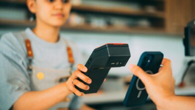 A cashier processes a contactless payment using a smartphone and card reader.