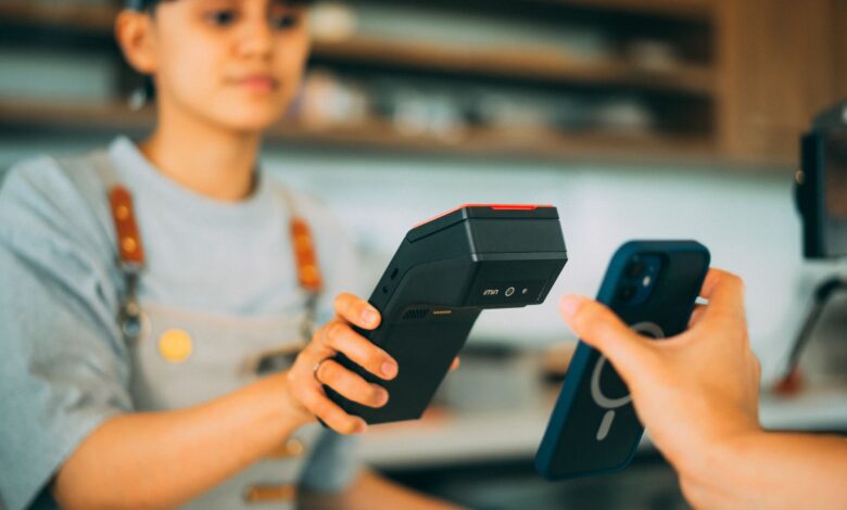 A cashier processes a contactless payment using a smartphone and card reader.