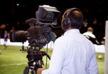 A cameraman filming a soccer match in a stadium, capturing the action on video.