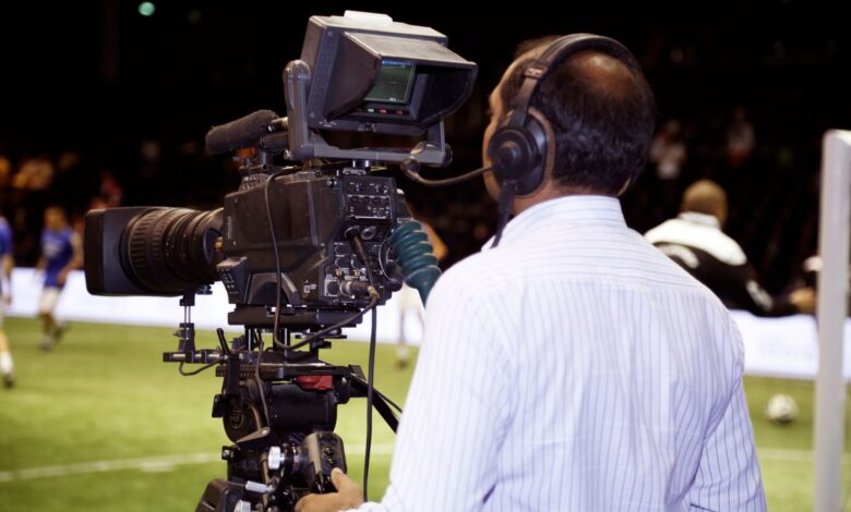 A cameraman filming a soccer match in a stadium, capturing the action on video.