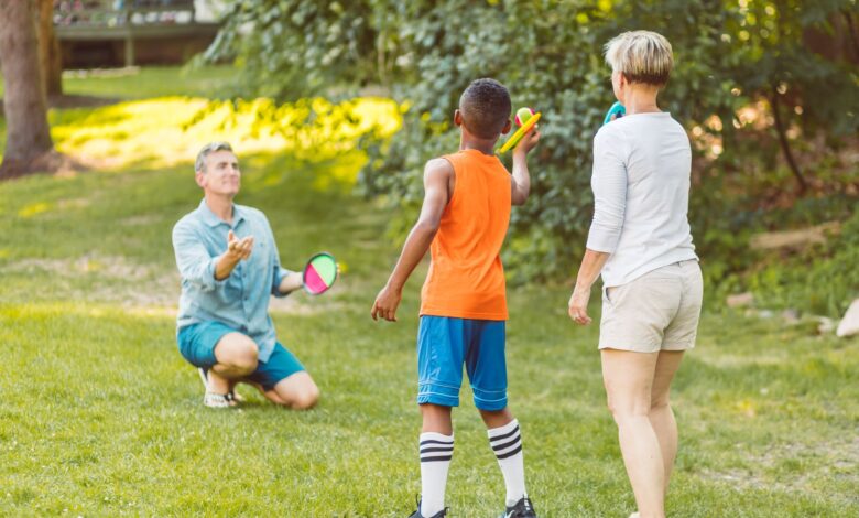 A family enjoying a game of velcro ball in a sunny park, showcasing togetherness and fun.