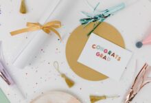 Flat lay of a graduation celebration arrangement with a congrats grad card, tassels, and confetti on a white surface.