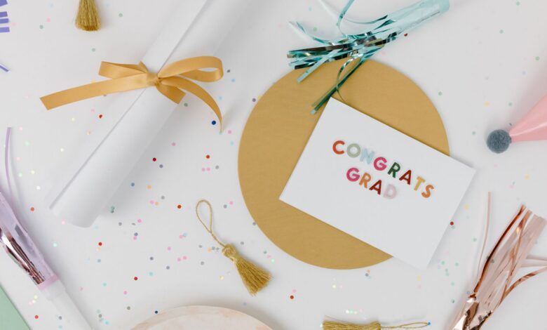 Flat lay of a graduation celebration arrangement with a congrats grad card, tassels, and confetti on a white surface.