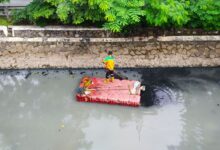 Man standing on raft cleaning a polluted river. Aerial view shows environmental challenges.