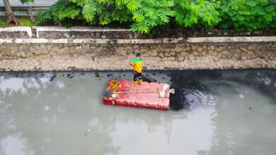 Man standing on raft cleaning a polluted river. Aerial view shows environmental challenges.