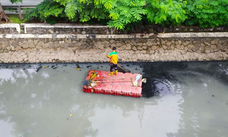 Man standing on raft cleaning a polluted river. Aerial view shows environmental challenges.
