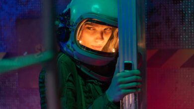 A woman astronaut in a helmet inside a sci-fi space vessel, surrounded by colorful lighting.